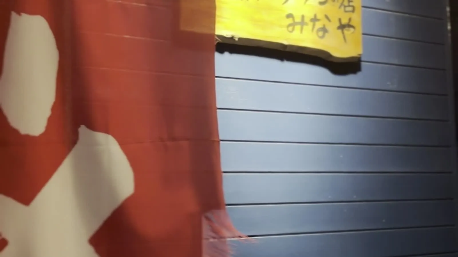 Entrance to みなや ramen shop in Haebaru, Okinawa — red noren curtain and hand-written shop sign