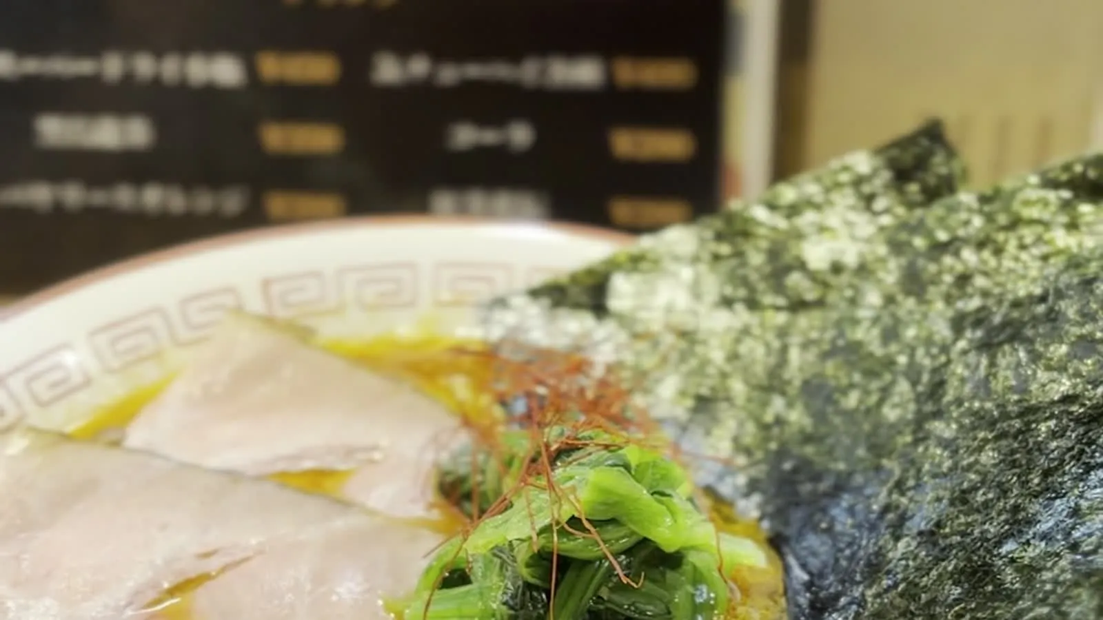 Tonkotsu ramen closeup at みなや, Haebaru — with Japanese menu board visible in background