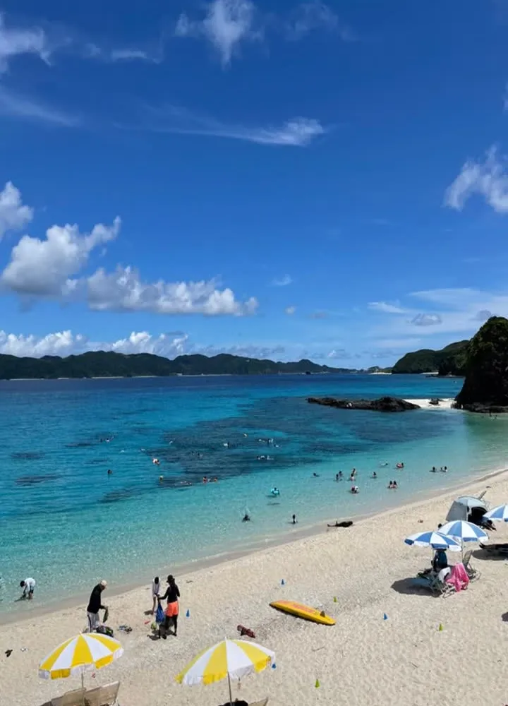 Zamami Island beach in August — turquoise water, white sand, beach umbrellas and swimmers under blue sky, Okinawa