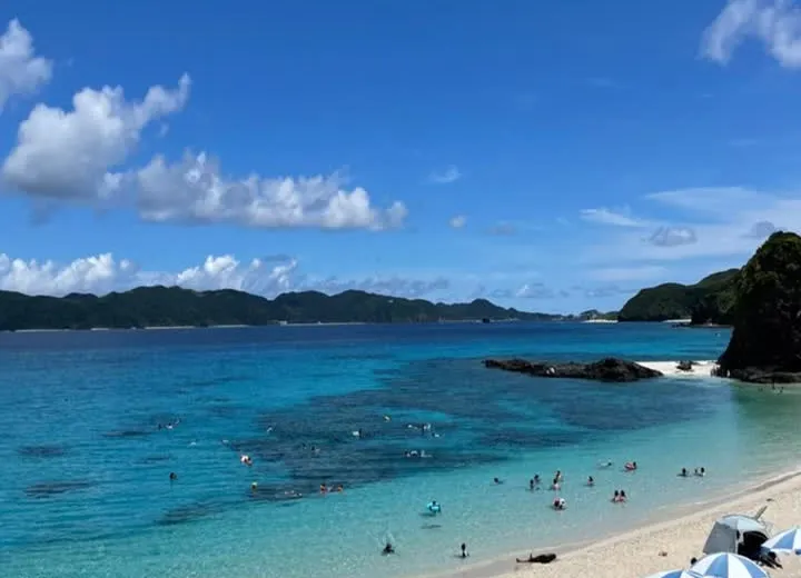 Zamami Island beach in August — turquoise water, white sand, beach umbrellas and swimmers under blue sky, Okinawa