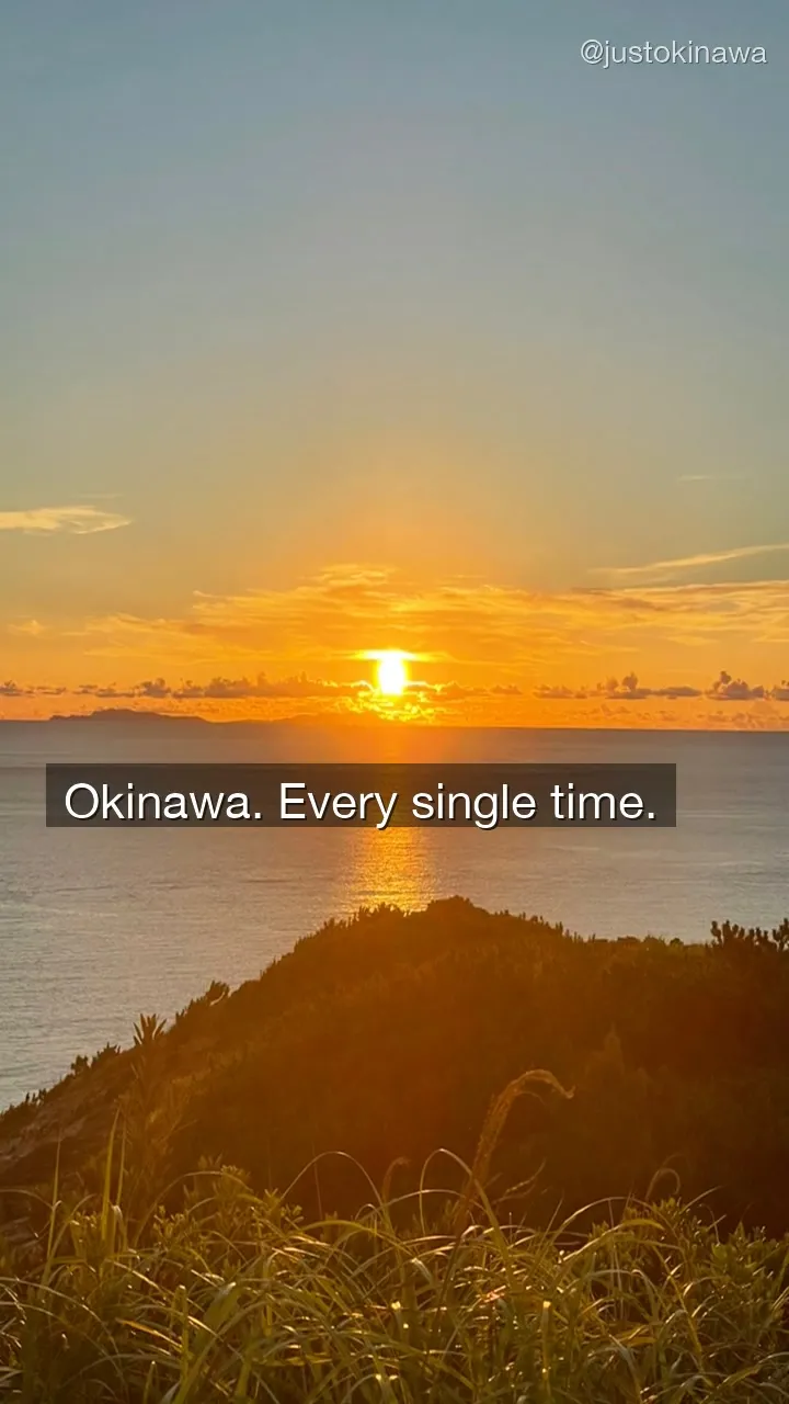 Sunset over Zamami Island — sun setting behind the hills, golden light reflected on the ocean, grass in the foreground