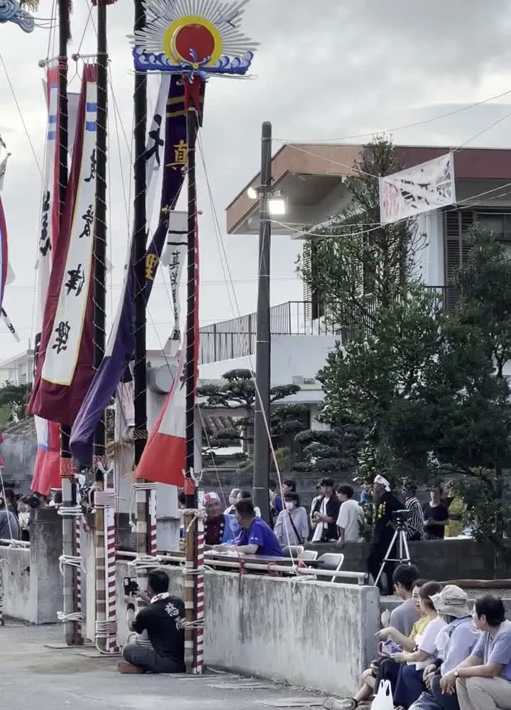 Hatakata ceremony at dusk during Hōnen Matsuri in Ishigaki Island — large decorated flag poles balanced by hand at the harvest festival