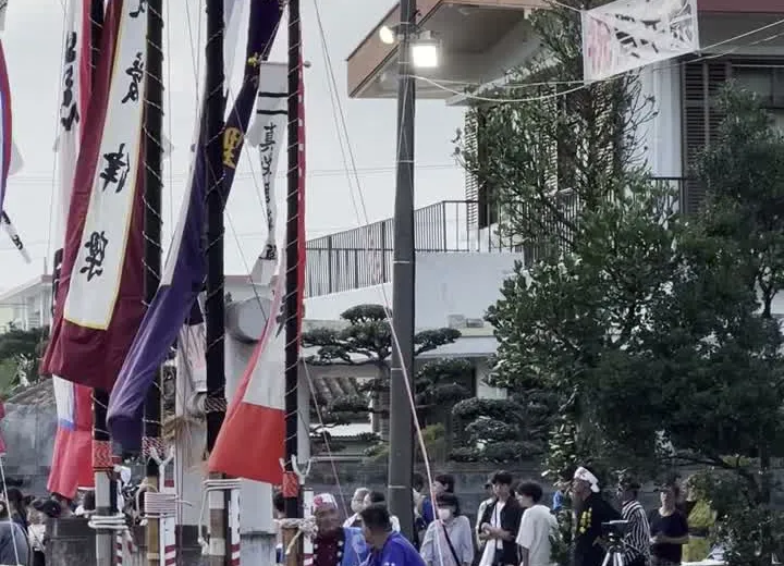 Hatakata ceremony at dusk during Hōnen Matsuri in Ishigaki Island — large decorated flag poles balanced by hand at the harvest festival